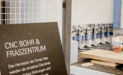 Links Schild mit Aufschrift CNC Bohr & Fräszentrum, rechts werden Bretter bearbeitet.