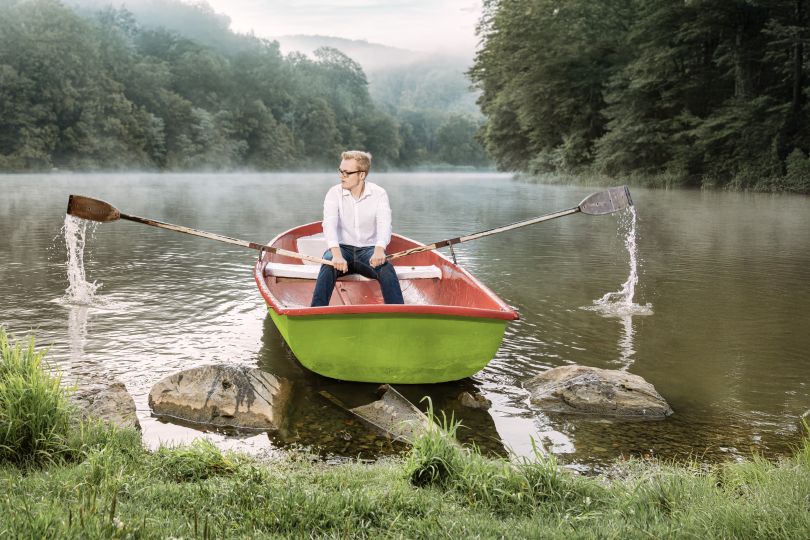 Ein junger Mann in weißem Hemd startet ein grünes Ruderboot in einem nebelverhangenen See