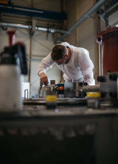 Arbeiter im weißen Schutzanzug beugt sich über Maschine