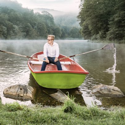 Mann rudert in Boot auf einem See vom Ufer weg