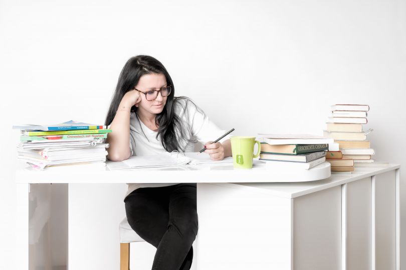 Frau sitzt am Schreibtisch und lernt, vor ihr Bücher und Block