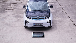 Schwarz-weißer BMW i3 hinter quadratischer, metallischer Ladeplatte