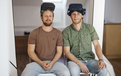 Zwei Männer sitzen auf Stühlen mit Virtal-Reality-Brillen auf der Stirn.