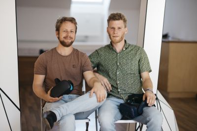 Zwei Männer sitzen auf Stühlen mit Virtal-Reality-Brillen in der Hand.