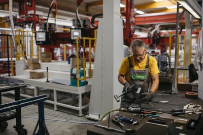 Mann mit Brille und Latzhose arbeitet mit Hammer in einer Produktionshalle