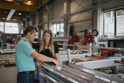 Florian Hampel zeigt Sigrid Merth in Produktionshall lange Metallteile
