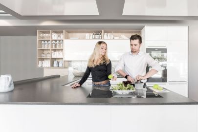 Ein Mann und eine Frau bereiten Salat zu. Der Mann presst eine Limette mit einer herkömmlichen Zitruspresse aus; die Frau hat eine Sprühvorrichtung in eine Limette gesteckt und zeigt dem Mann, wie es auf diese Weise einfacher geht.