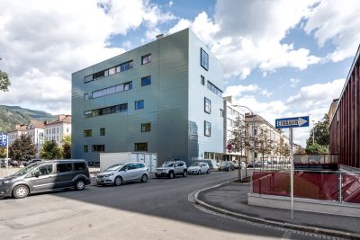 Außenansicht von modernem Gebäude, davor Straße mit parkenden Autos
