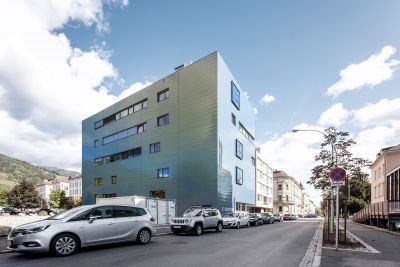 Außenansicht von modernem Gebäude, davor Straße mit parkenden Autos