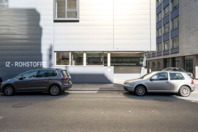 Außenansicht von Gebäude, davor Straße mit parkenden Autos.