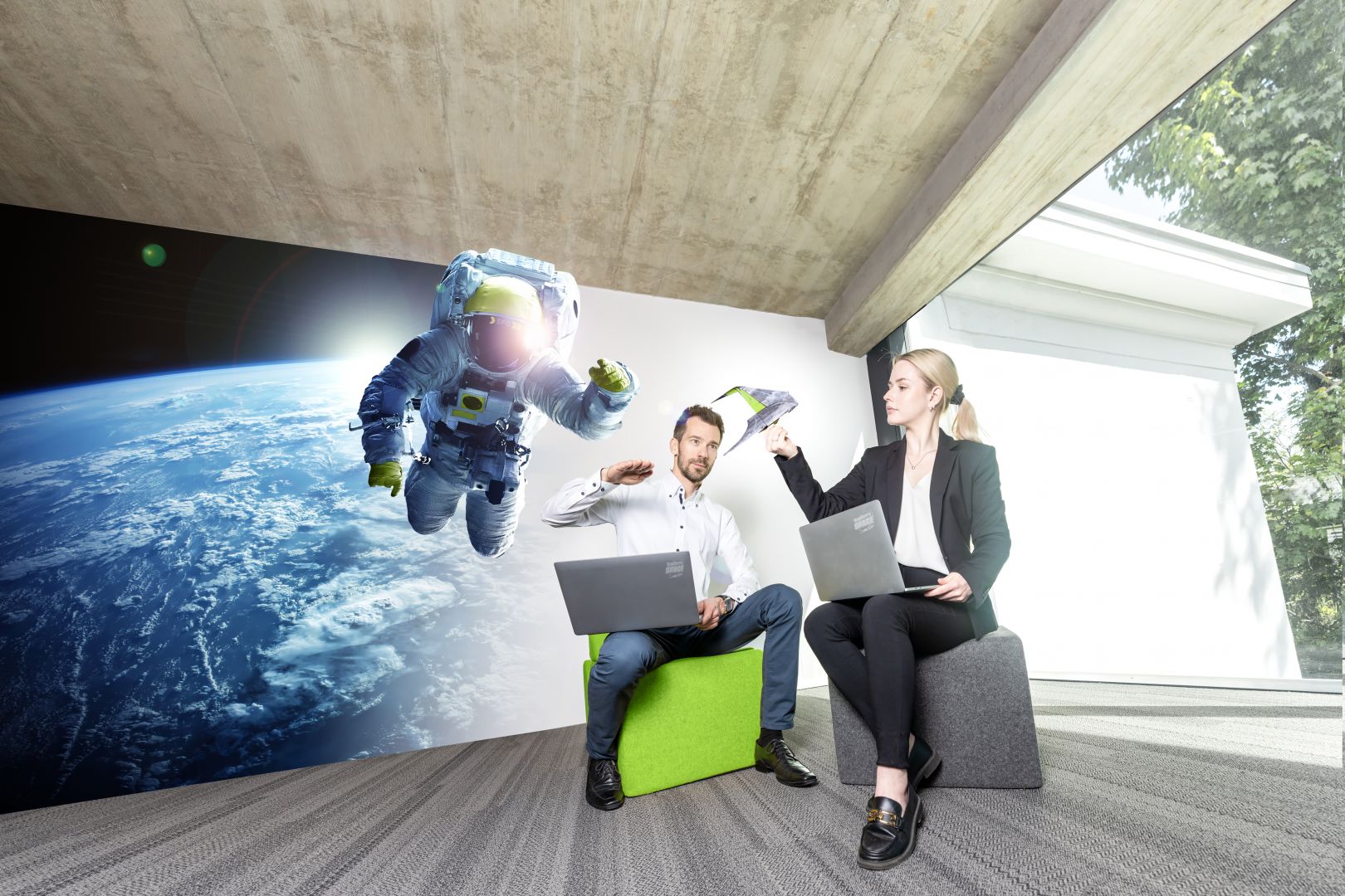 Mann und Frau mit Laptop, im Hintergrund ein Astronaut im Weltall