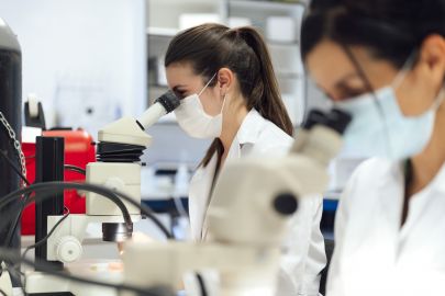 Wissenschaftlerinnen schauen durch ein Mikroskop, während sie medizinische Proben im Labor untersuchen.