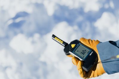 Schnee mit behandschuhter Hand, die ein Lawinenverschüttetenmessgerät hält
